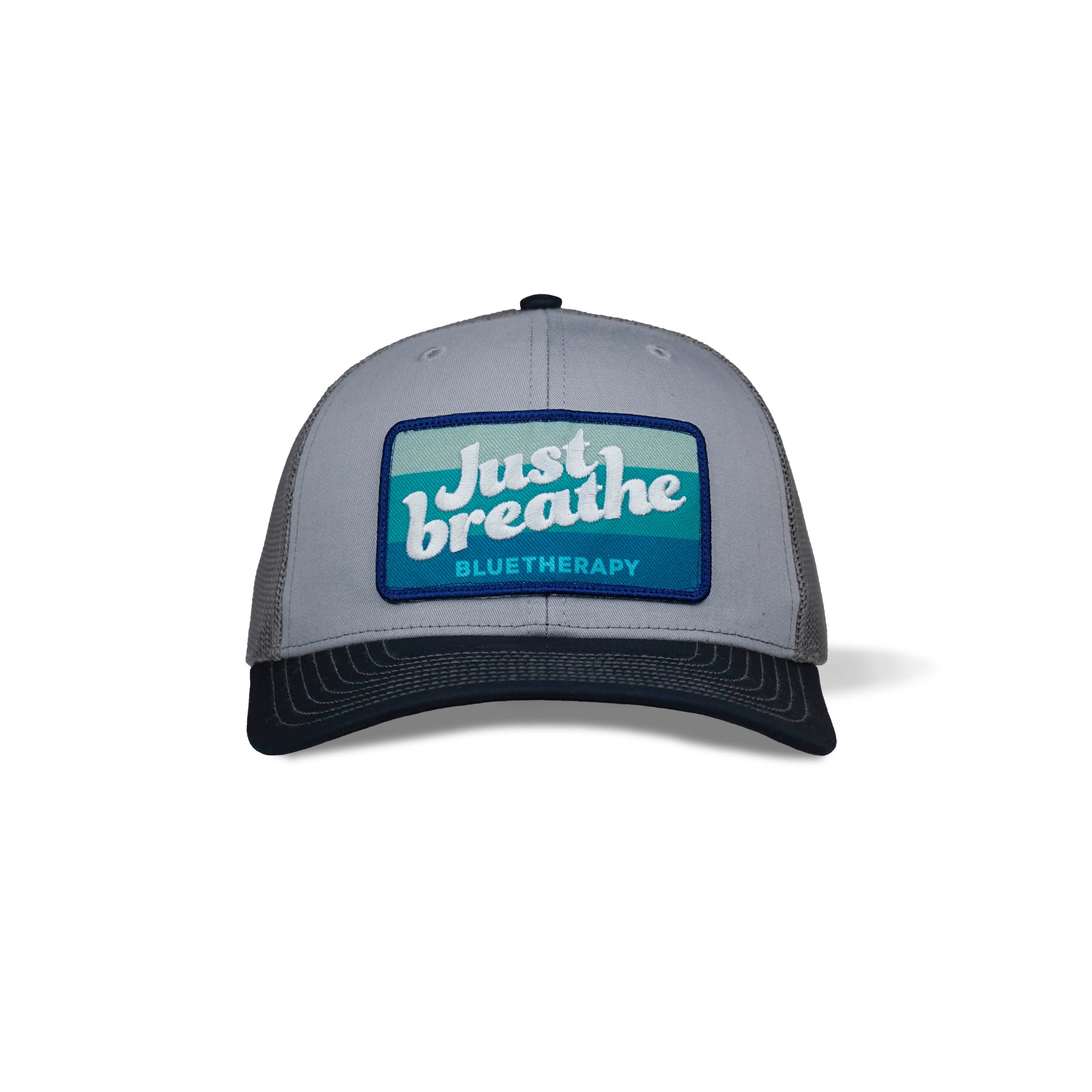 3-qtr view of trucker hat with a navy curved brim and a white embroidered text 'Just Breathe' on a blue blended patch