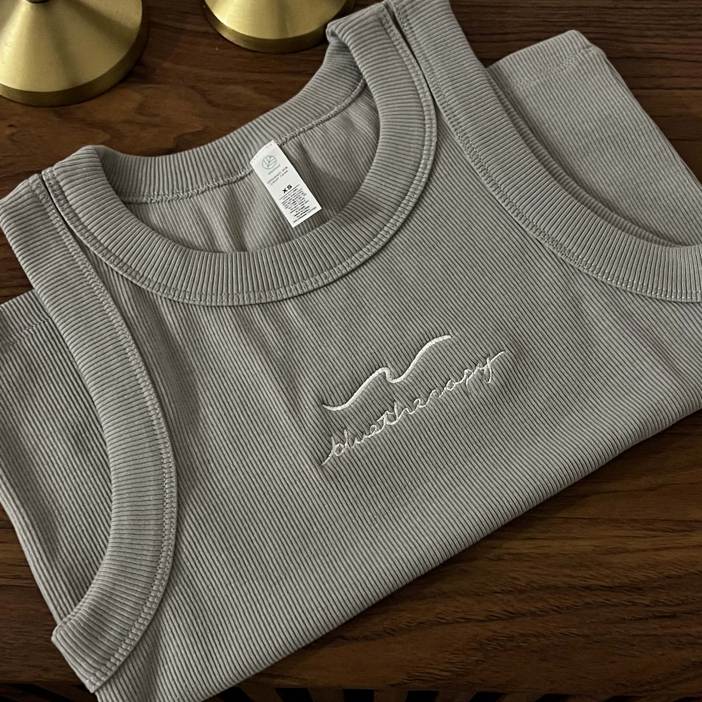 Gray ribbed crop BlueTherapy Wave tank top with embroidered wave art on the front, folded, on top of wooden dresser