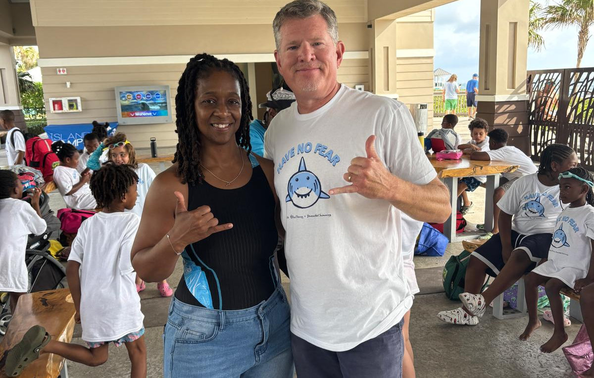 Tom from BlueTherapy and Shana from Diversified Swimming posing together in at a beach pavilion with children from the spring swim camp in the background