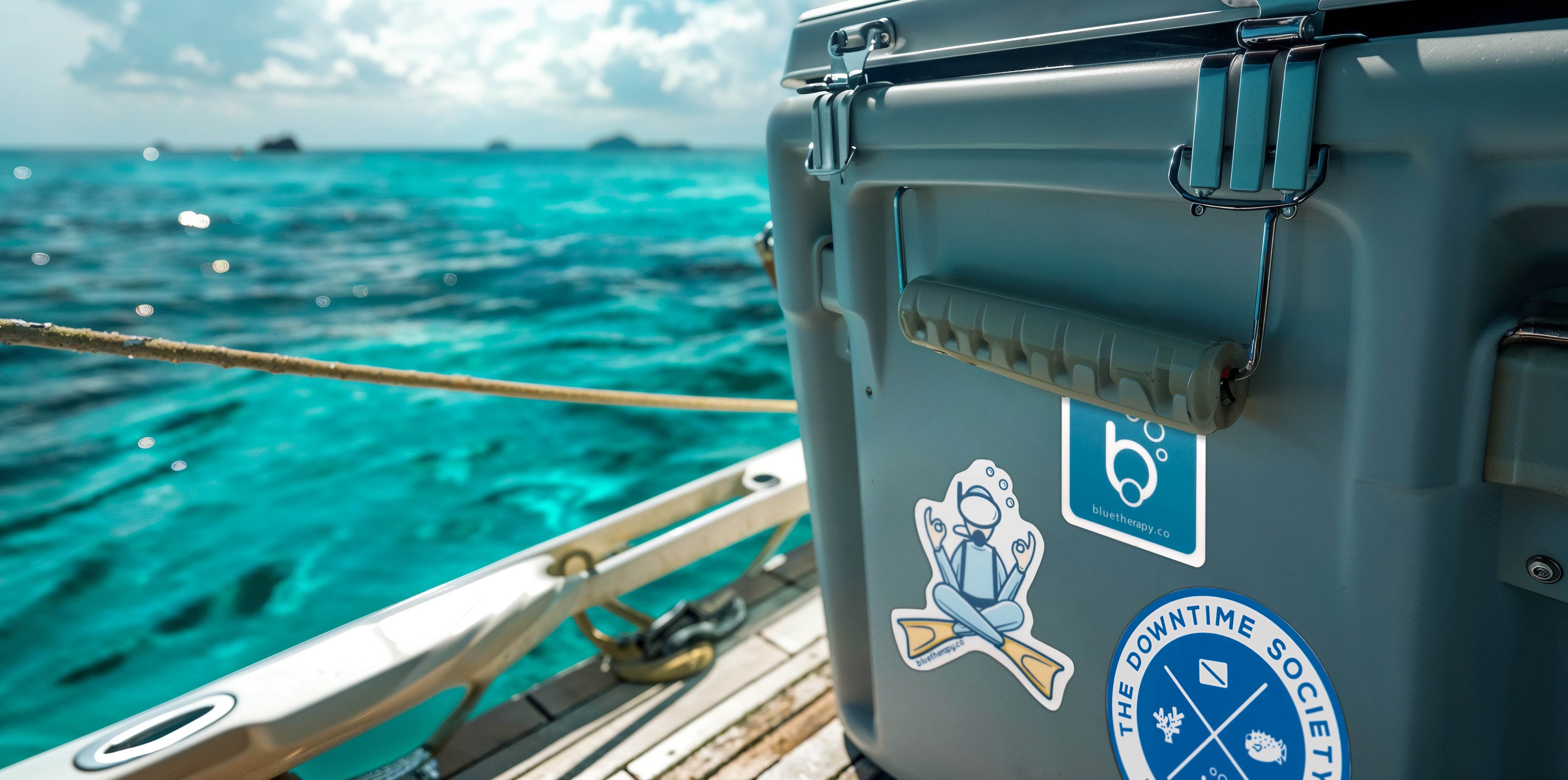 BlueTherapy stickers applied to cooler on boat, featuring zen diver, Downtime Society, and bubble b brand logo designs against ocean backdrop